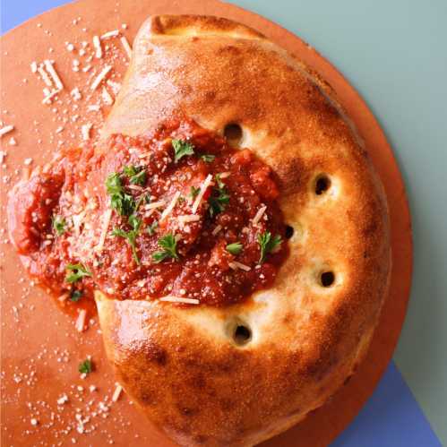 A golden calzone filled with cheese, served with marinara sauce and garnished with parsley and grated cheese.