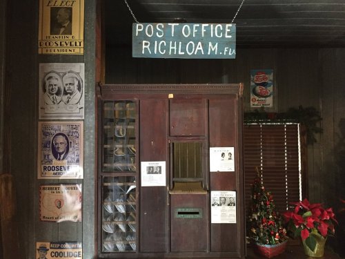 Interior of a historic post office in Richloam, Florida, featuring a wooden counter and vintage political posters.