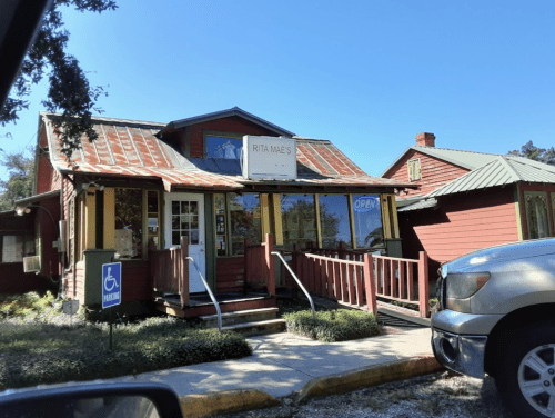 A quaint restaurant with a red exterior and a sign reading "Rita Mae's," featuring a ramp and outdoor seating.