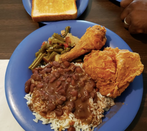 A blue plate with rice, brown beans, fried chicken, green beans, and a slice of toast in the background.