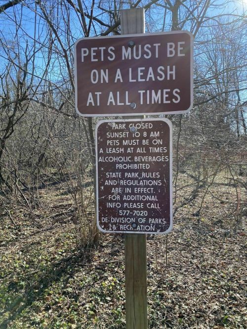 Sign indicating park rules: pets must be leashed, park closed at sunset, no alcohol, contact info provided.