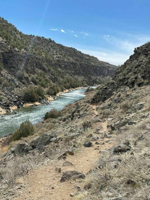 A winding river flows through a rocky canyon, surrounded by green hills and a clear blue sky.