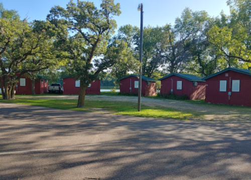 A row of red cabins surrounded by trees and grass, with a clear blue sky above.