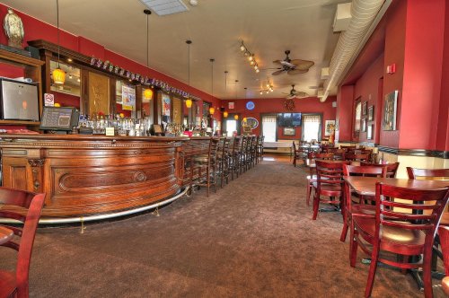 A warm, inviting bar area with wooden furnishings, a long counter, and empty tables in a cozy restaurant setting.