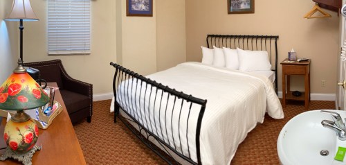 Cozy hotel room featuring a bed, chair, lamp, and sink, with warm colors and simple decor.