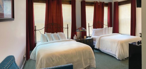 Cozy hotel room with two beds, red curtains, and a lamp, featuring a green carpet and a seating area.