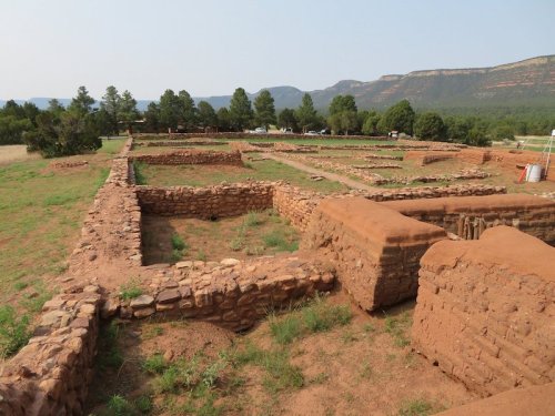Ruins of ancient stone structures surrounded by greenery and mountains in the background.
