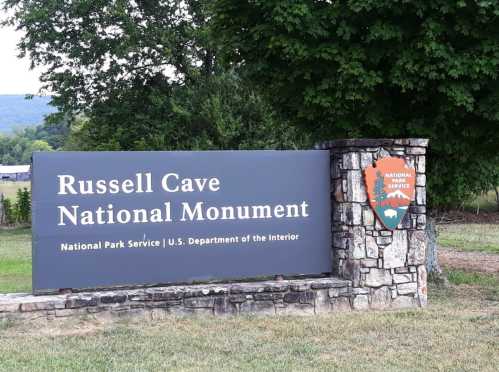 Sign for Russell Cave National Monument, featuring the park's name and logo, surrounded by greenery.