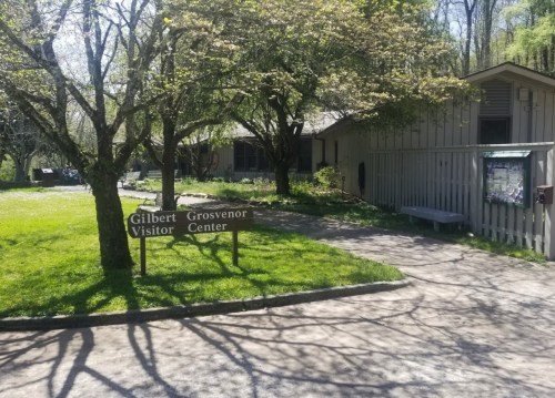 Sign for Gilbert Visitor Center in a green, tree-lined area with a building in the background.