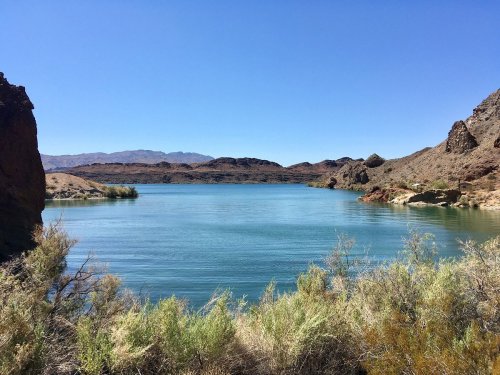 A serene lake surrounded by rocky hills and sparse vegetation under a clear blue sky.