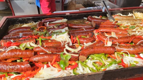 A large grill filled with various sausages and colorful bell peppers and onions, sizzling and ready to serve.
