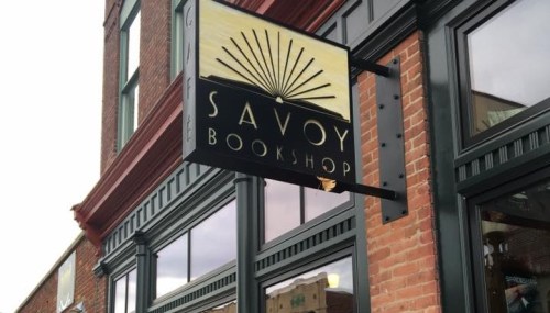Sign for Savoy Bookshop, featuring a sunburst design, mounted on a brick building.