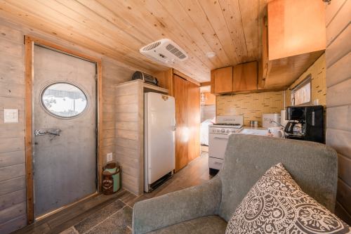 Cozy interior of a tiny home featuring a kitchen, a door, and a comfortable chair with a decorative pillow.