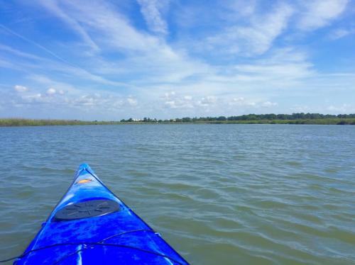 A blue kayak on calm water, with a scenic view of grassy banks and a blue sky filled with clouds.