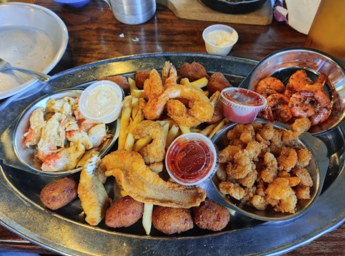 A large metal platter filled with various fried seafood, including shrimp, fish, and hushpuppies, with dipping sauces.