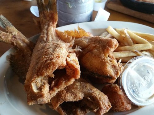 A plate of fried fish and fries, served with a small cup of dipping sauce.