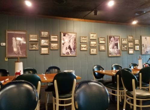 Interior of a restaurant featuring blue walls adorned with framed black-and-white photos, with empty tables and chairs.
