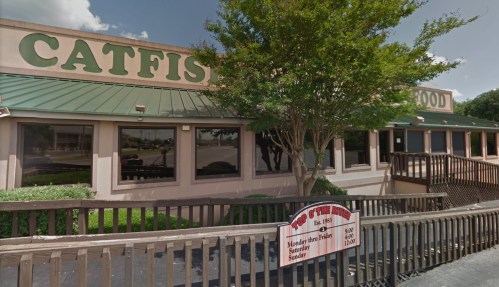 Exterior of a restaurant named "Catfish," featuring a green roof and a wooden deck with a sign for hours of operation.