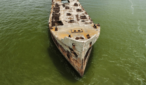 Aerial view of a rusted shipwreck partially submerged in green water.