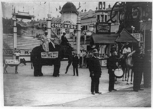 A historic scene featuring an elephant with riders, police officers, and a carnival backdrop in an amusement park.