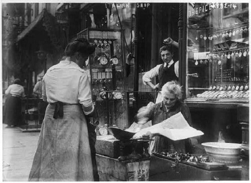 A historic street scene with women working at a market, selling goods, and a man observing in the background.