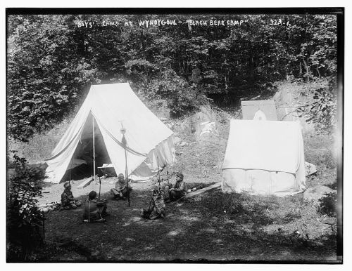 Boys' camp at Wyoming, featuring tents and campers gathered around a fire in a wooded area.