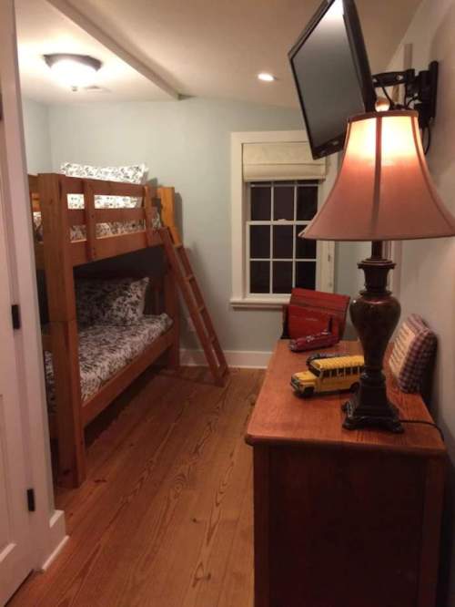 A cozy bedroom featuring a wooden bunk bed, a lamp, a dresser, and a wall-mounted TV.