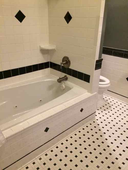 A bathroom featuring a white and black tiled bathtub, shower, and toilet with a checkered floor design.