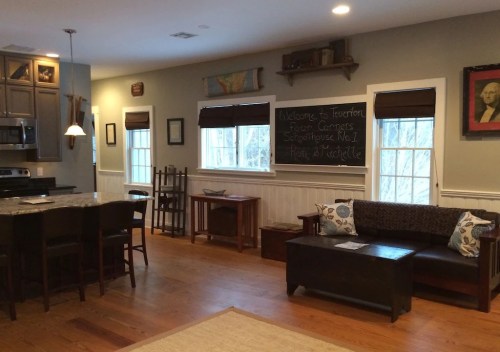 Cozy living space with a sofa, wooden furniture, and a kitchen area, featuring large windows and warm lighting.