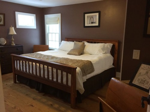 Cozy bedroom featuring a wooden bed, white linens, a nightstand, and warm brown walls.