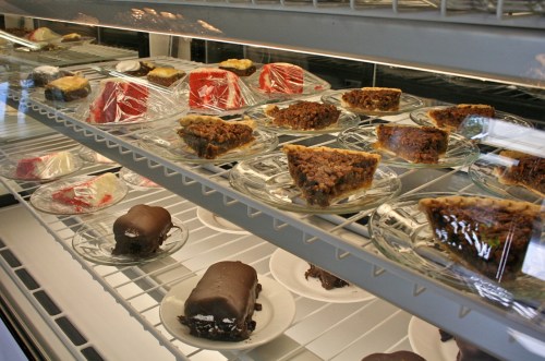 A display case filled with various desserts, including cakes and pastries, covered with plastic wrap.