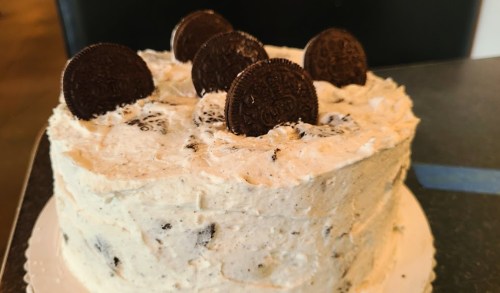 A round cake with cream frosting and Oreo cookies on top, placed on a white cake board.