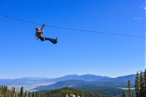 A person zip-lining over a mountainous landscape under a clear blue sky.