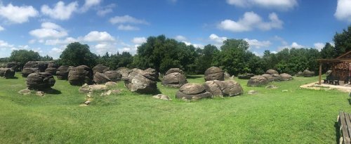 A panoramic view of large, rounded boulders scattered across a green field under a blue sky with fluffy clouds.