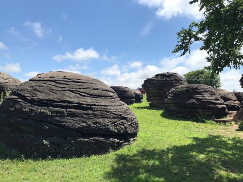 Large, rounded rock formations scattered across a grassy field under a blue sky with fluffy clouds.