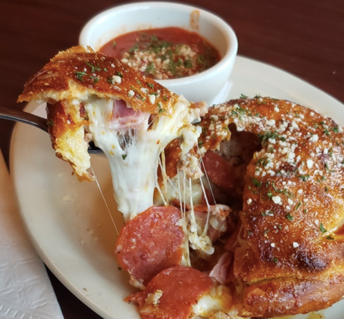 A cheesy stuffed bread with pepperoni, pulled apart, next to a small bowl of marinara sauce.