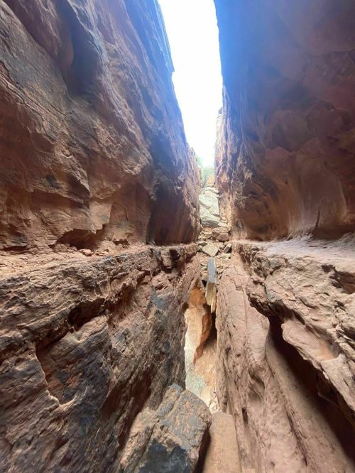 Narrow canyon walls of red rock with a bright sky visible at the top, creating a dramatic natural landscape.