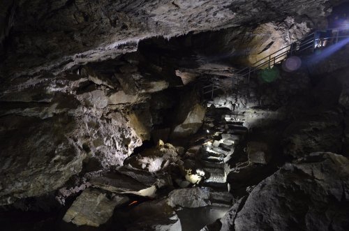 Dimly lit cave interior with rocky formations and a staircase leading deeper into the cavern.