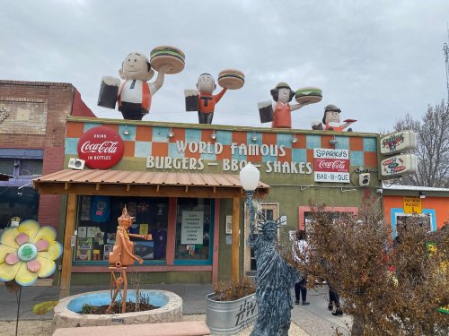 Colorful restaurant exterior featuring cartoonish figures holding burgers, with signs for burgers, BBQ, and shakes.