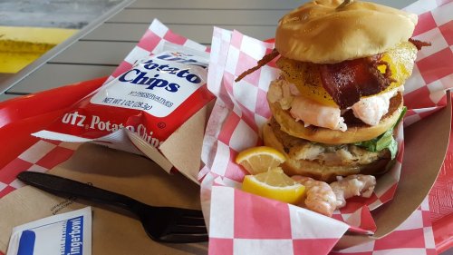 A towering burger with layers of shrimp, bacon, and toppings, served with Utz potato chips and lemon wedges.