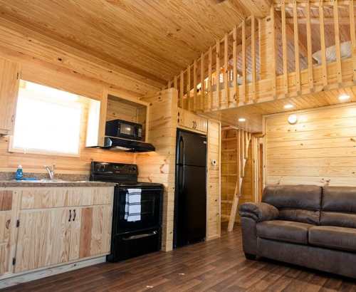 Cozy wooden interior of a cabin featuring a kitchen, living area, and a lofted sleeping space.