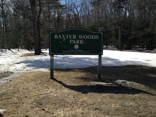 Sign for Baxter Woods Park, surrounded by snow and trees, indicating it's a city park managed by the Department of Parks and Recreation.