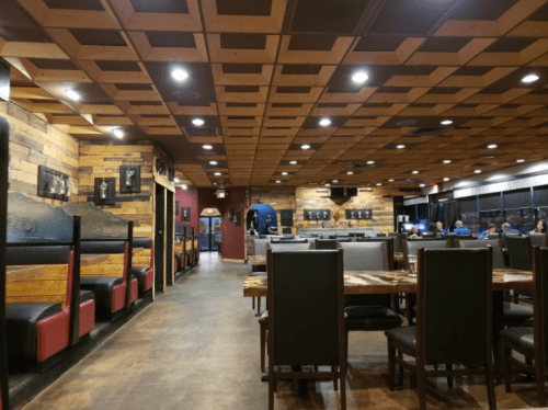 Interior of a restaurant featuring wooden decor, booths, and tables, with warm lighting and a cozy atmosphere.