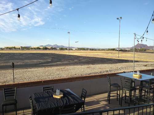 View from a restaurant patio overlooking an empty airstrip with mountains in the background and an airplane in the sky.