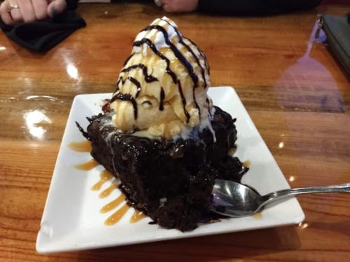 A decadent chocolate brownie topped with vanilla ice cream, whipped cream, and chocolate drizzle on a white plate.