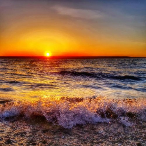 A vibrant sunset over the ocean, with waves gently lapping at the shore and a colorful sky.