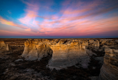A stunning sunset over rugged rock formations and a vast landscape, with vibrant pink and purple clouds in the sky.