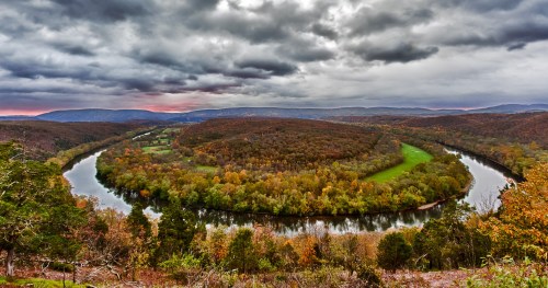 A winding river flows through a colorful forested landscape under a cloudy sky.