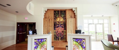 A bright reception area featuring a stained glass backdrop and wooden accents, with two front desks.