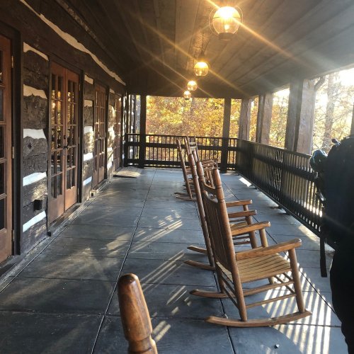 A rustic porch with wooden rocking chairs and lanterns, surrounded by autumn foliage.